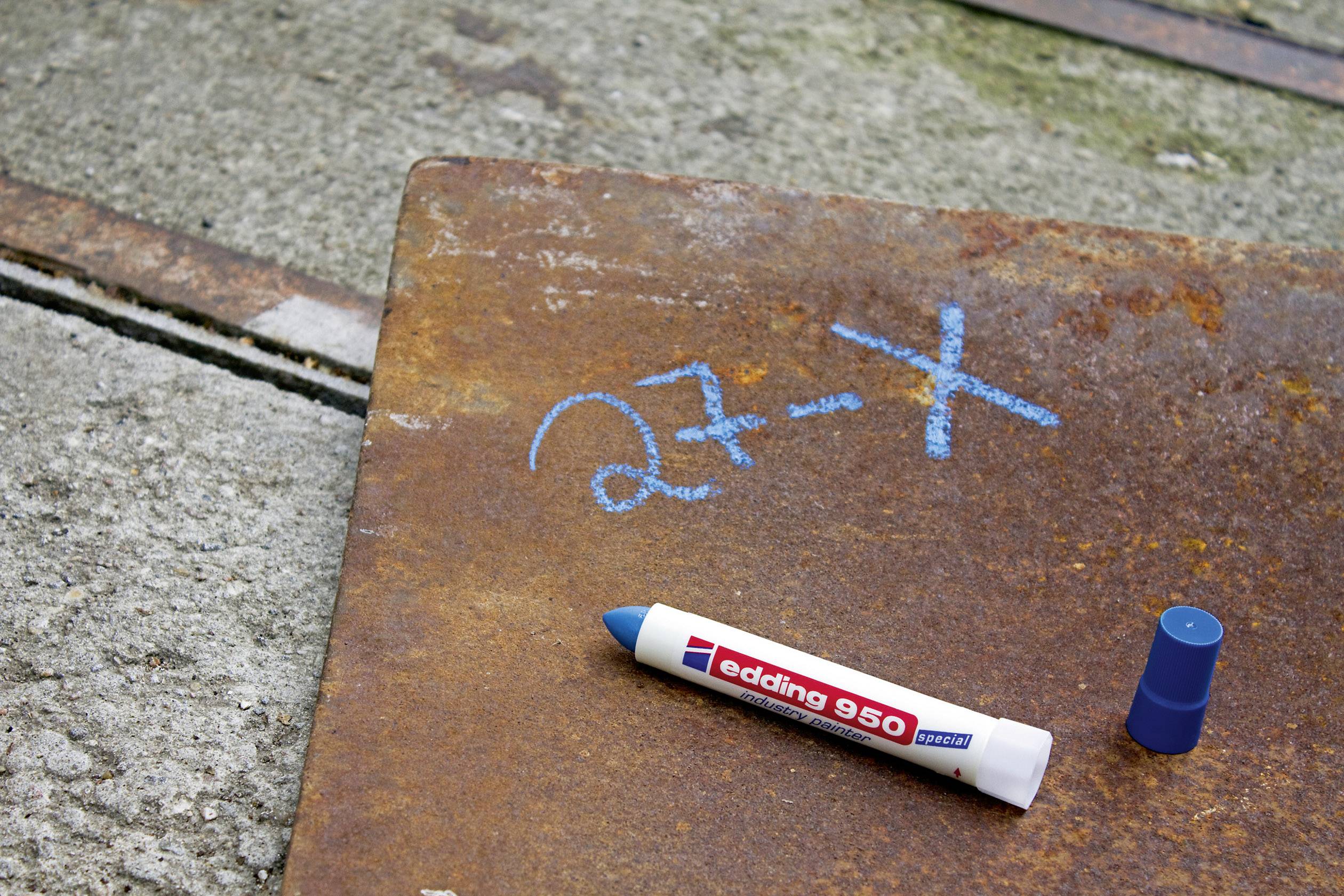 Ein Metallstück auf Betonboden, mit blauer Kreide beschriftet: '27-X'. Ein geöffneter blauer Filzstift liegt daneben.
