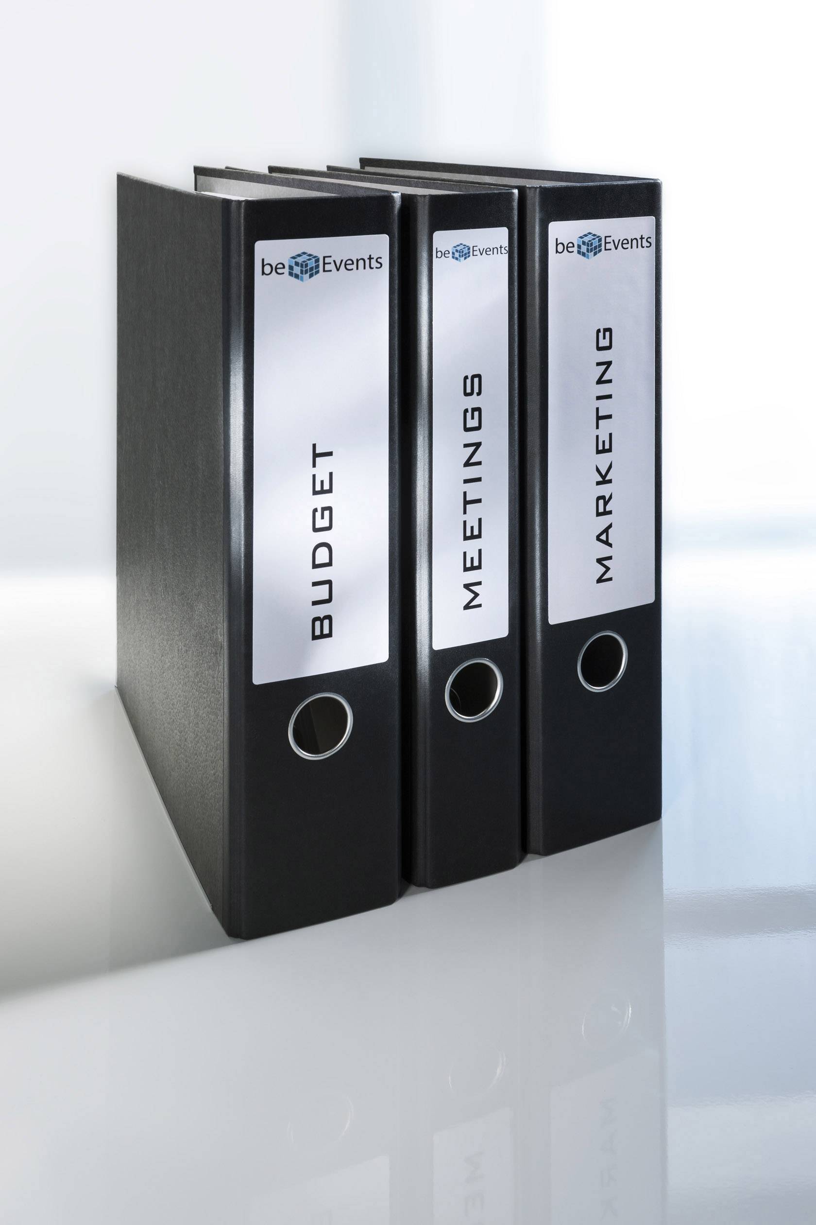 Drei schwarze Ordner mit den Beschriftungen 'Budget', 'Meetings', und 'Marketing' stehen nebeneinander auf einem weißen Tisch.