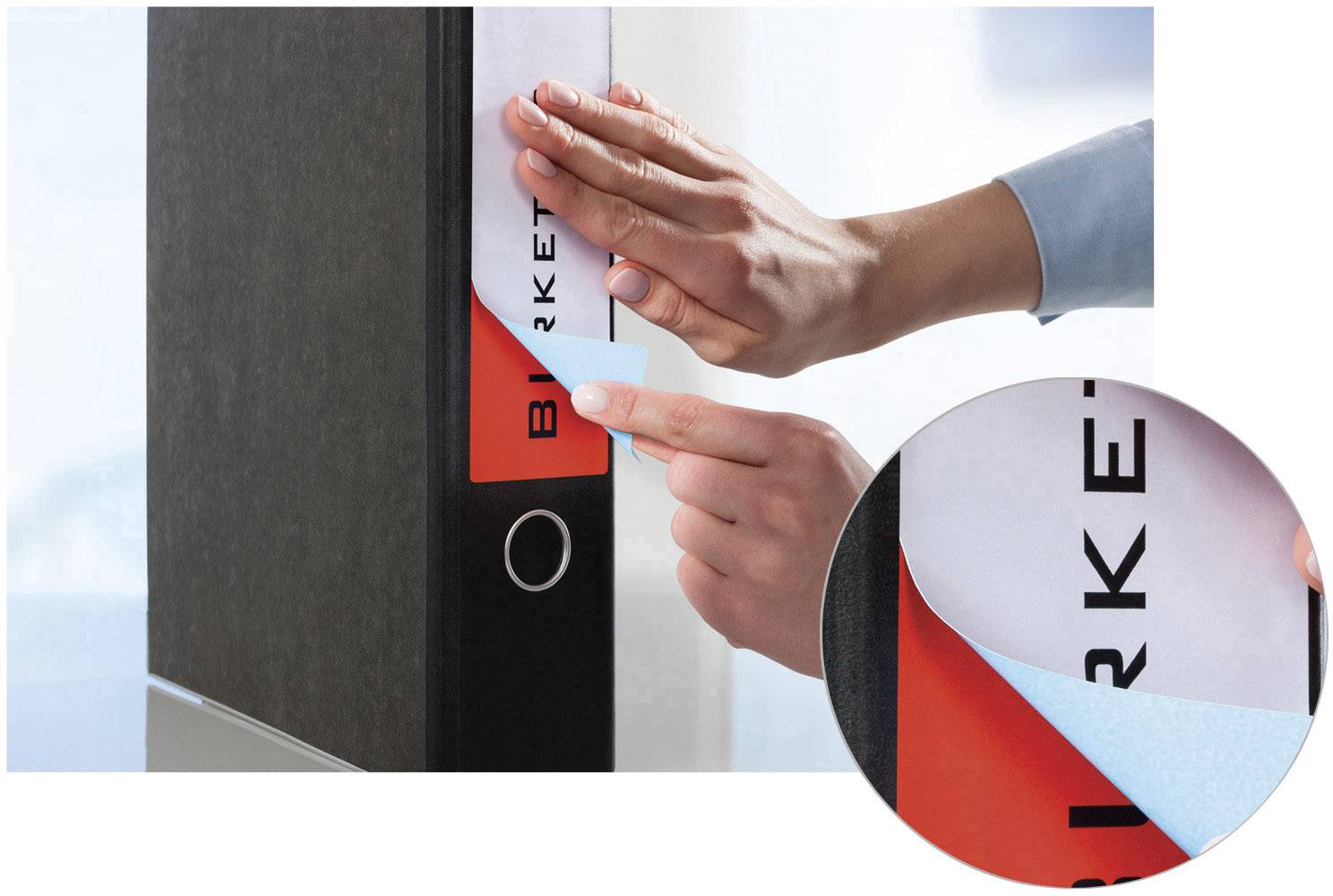 Eine Person klebt ein neues Etikett auf einen schwarzen Ordner. Ein vergrößerter Ausschnitt zeigt die entfernbare Etikettenstruktur.