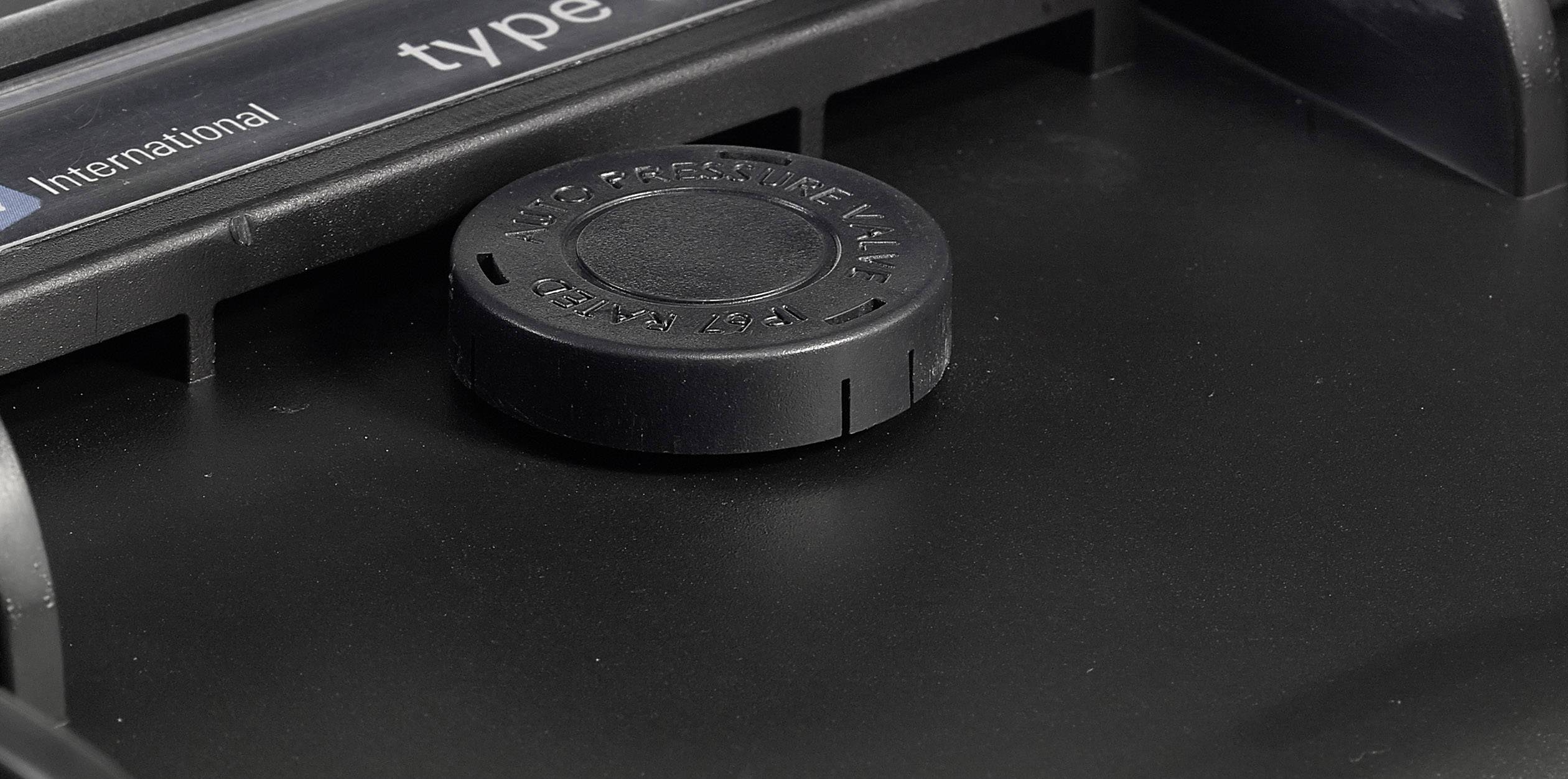 Schwarzes Kunststoff-Bauteil in Nahaufnahme, mit einem zentral angeordneten runden Verschlussdeckel.