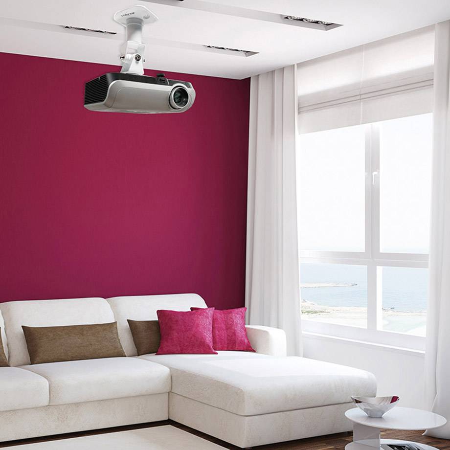 Wohnzimmer mit weißem Sofa, roten Kissen und einem Projektor an der Decke. Ein großes Fenster bietet Blick auf das Meer.