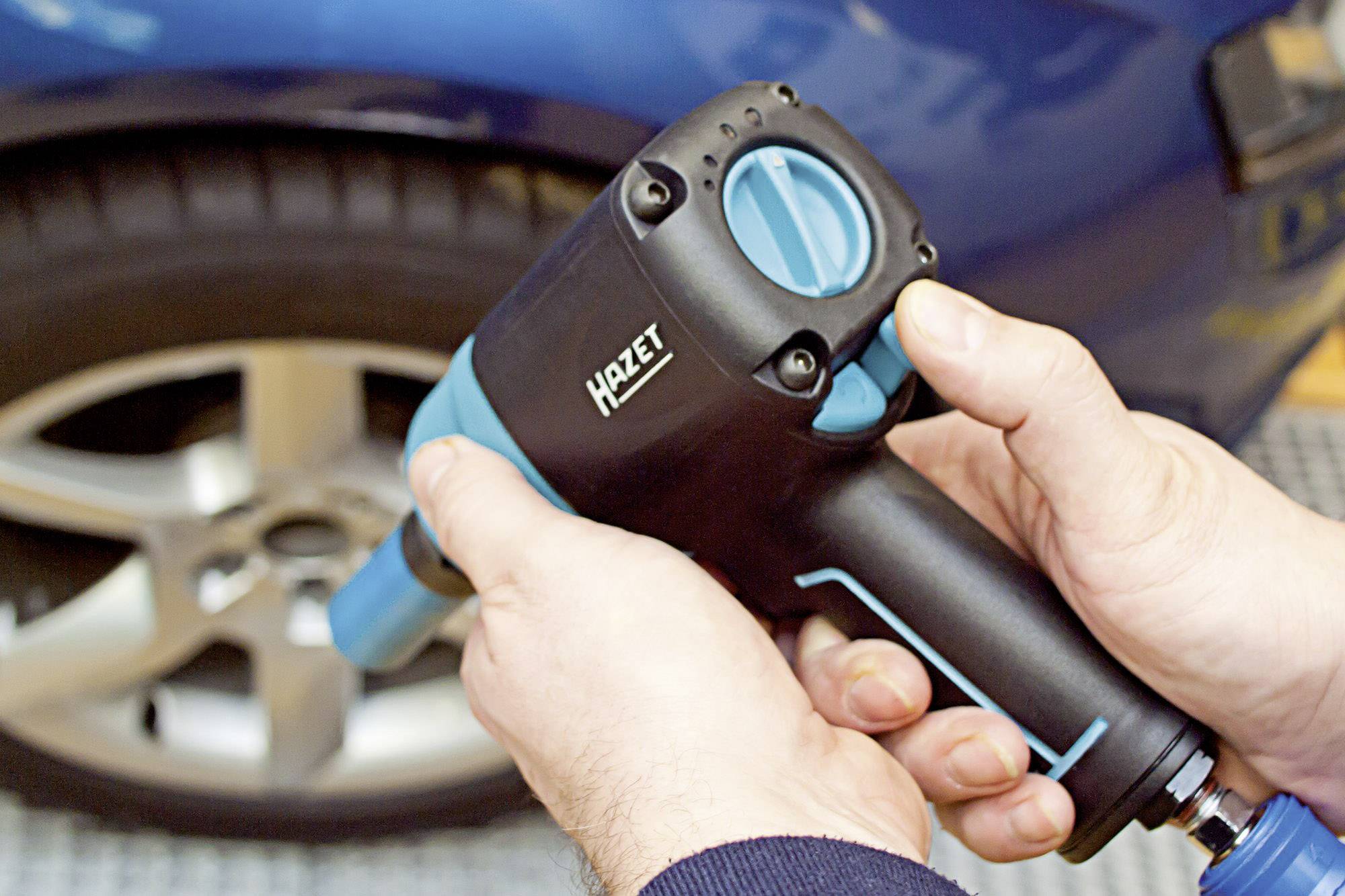 Eine Person hält einen Druckluft-Schlagschrauber, um ein Rad an einem blauen Auto zu befestigen oder zu entfernen. Der Schrauber ist schwarz und blau.
