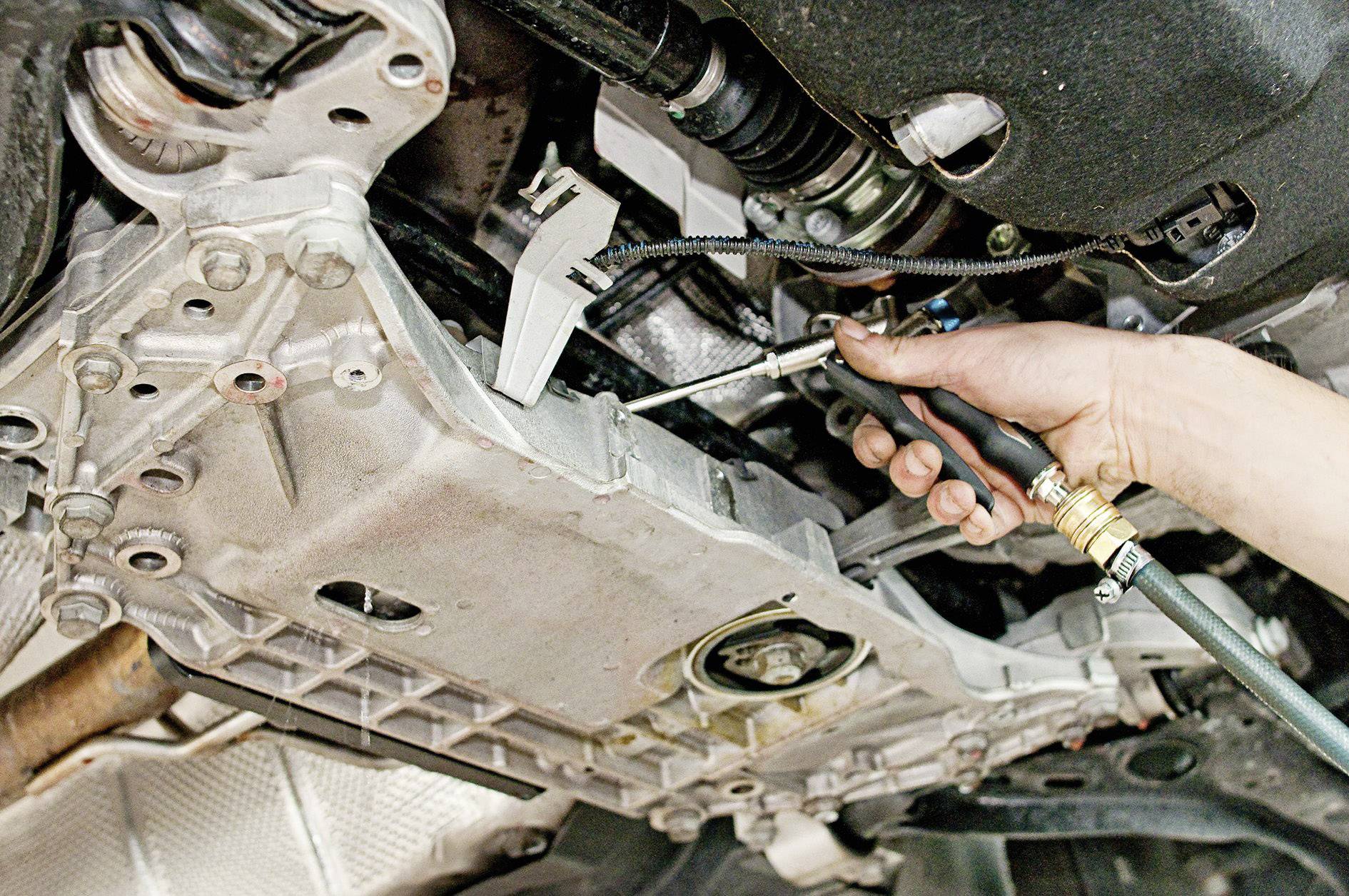 Eine Person führt eine Reparatur oder Wartung an einem Automotor durch. Ein Werkzeug wird an einer Metallkomponente angesetzt.