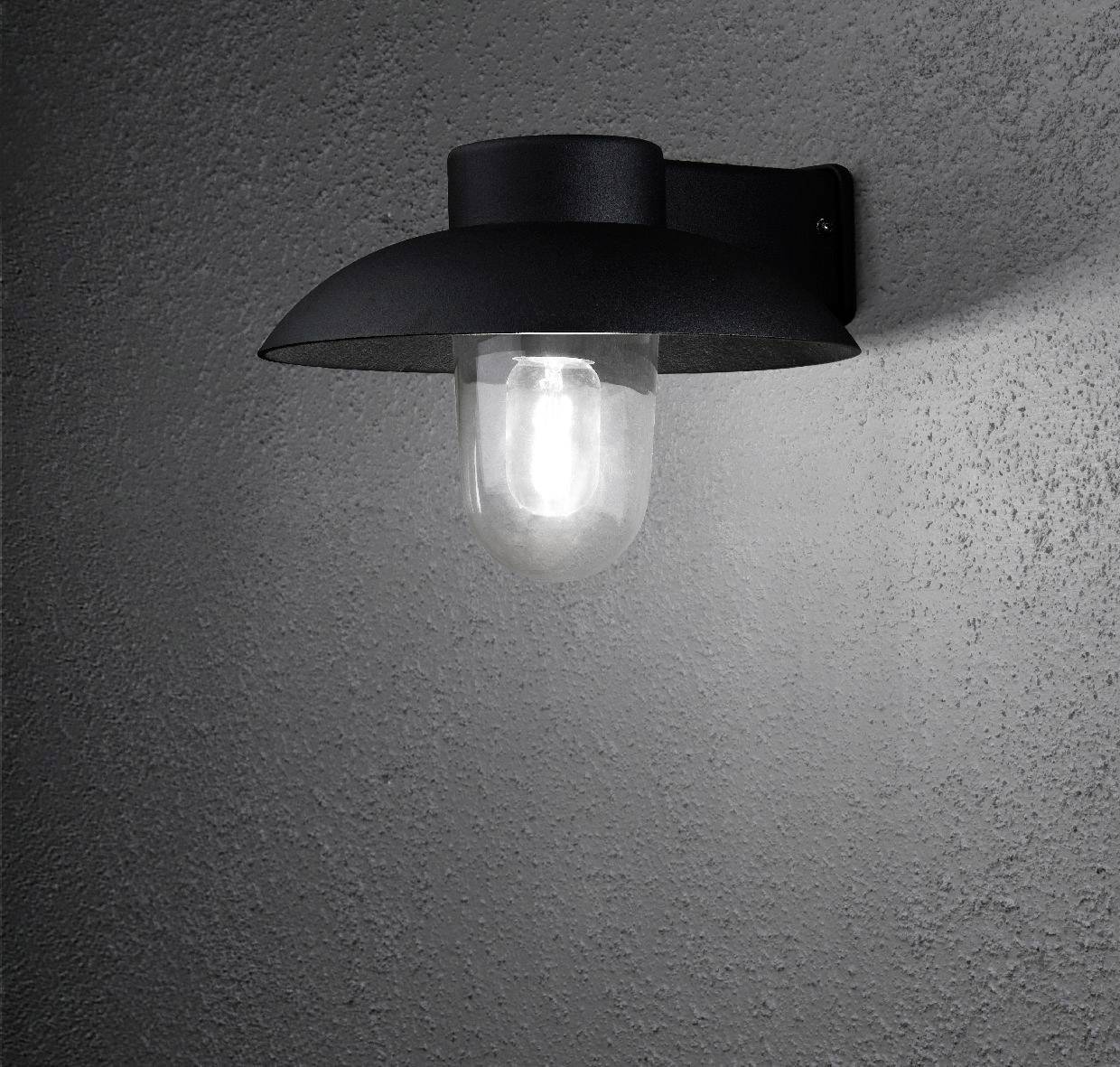 Eine schwarze Wandleuchte mit Glasabdeckung strahlt auf grauem Hintergrund.