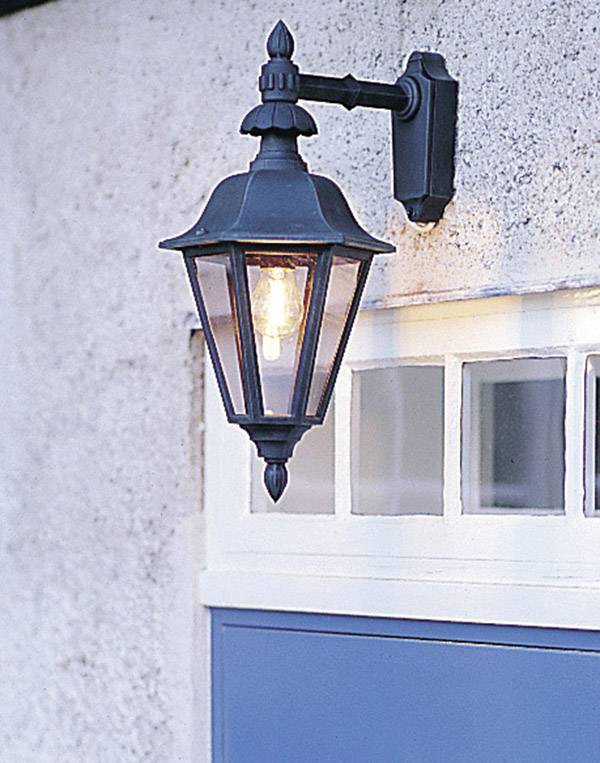 Außenwandleuchte in Laternenform an einer Wand montiert, leuchtet und beleuchtet den darunterliegenden blauen Bereich.
