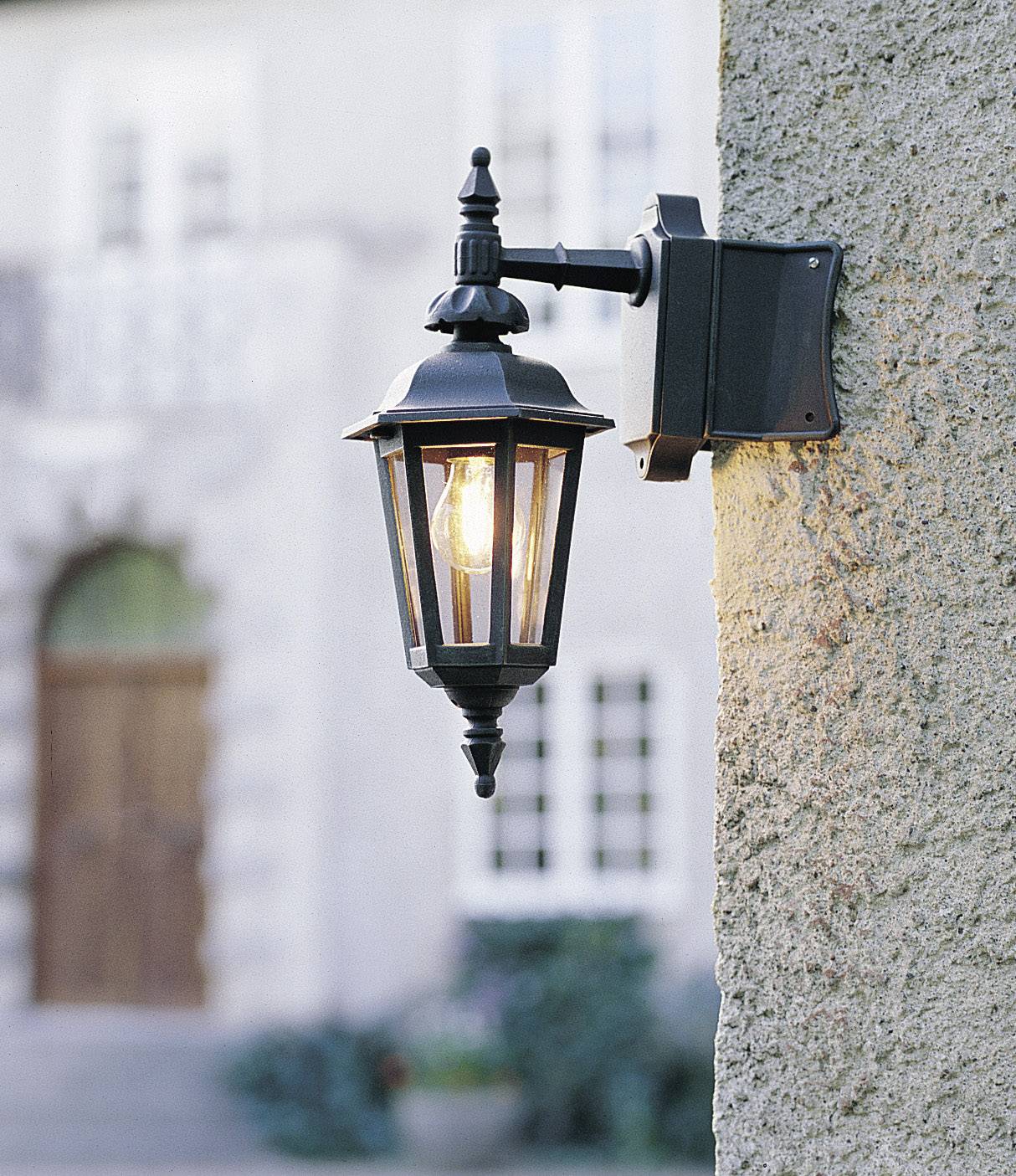 Außenwandlaterne aus schwarzem Metall mit klassischem Design, befestigt an einer Steinmauer, leuchtet auf einen Eingang mit Holztür.