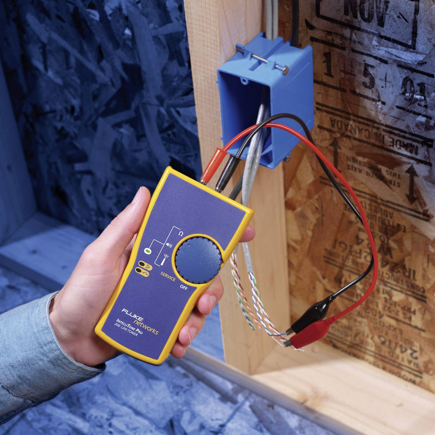 Ein Multimeter prüft Spannung in einer elektrischen Box. Eine Person hält das Gerät und die Sonden sind an Drähte angeschlossen.