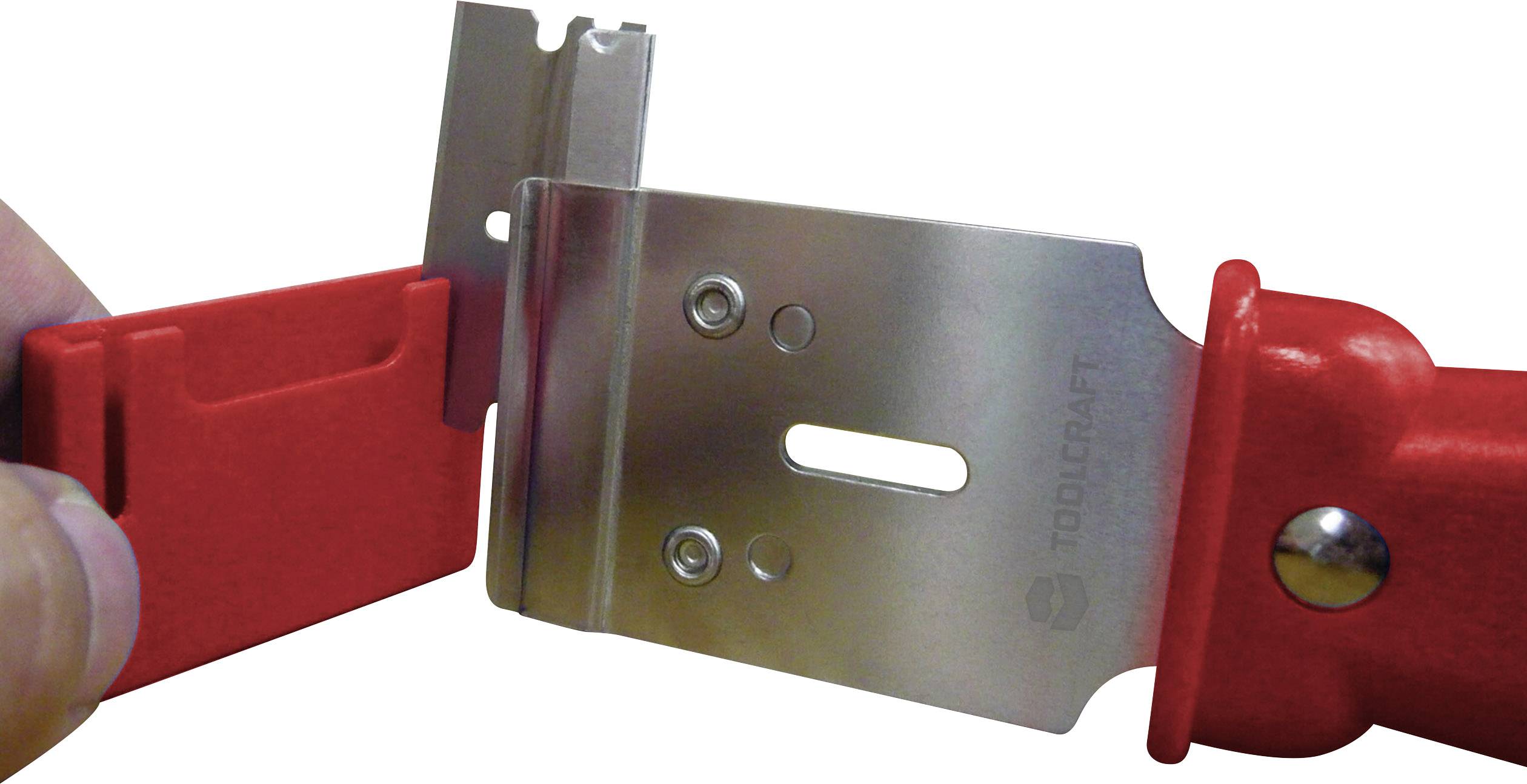 Eine Hand hält einen roten Sicherheitsklingenhalter mit eingesetzter Klinge; die Klinge ist metallisch und rechteckig.