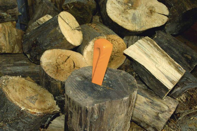Ein orangener Holzspalter steckt in einem Baumstamm, umgeben von mehreren gespaltenen Holzscheiten.