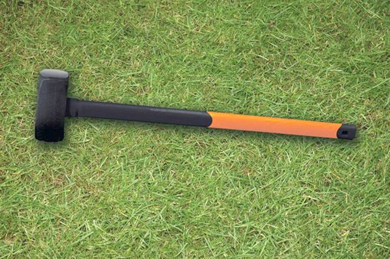 Ein Vorschlaghammer mit orangem und schwarzem Griff liegt auf grünem Gras.