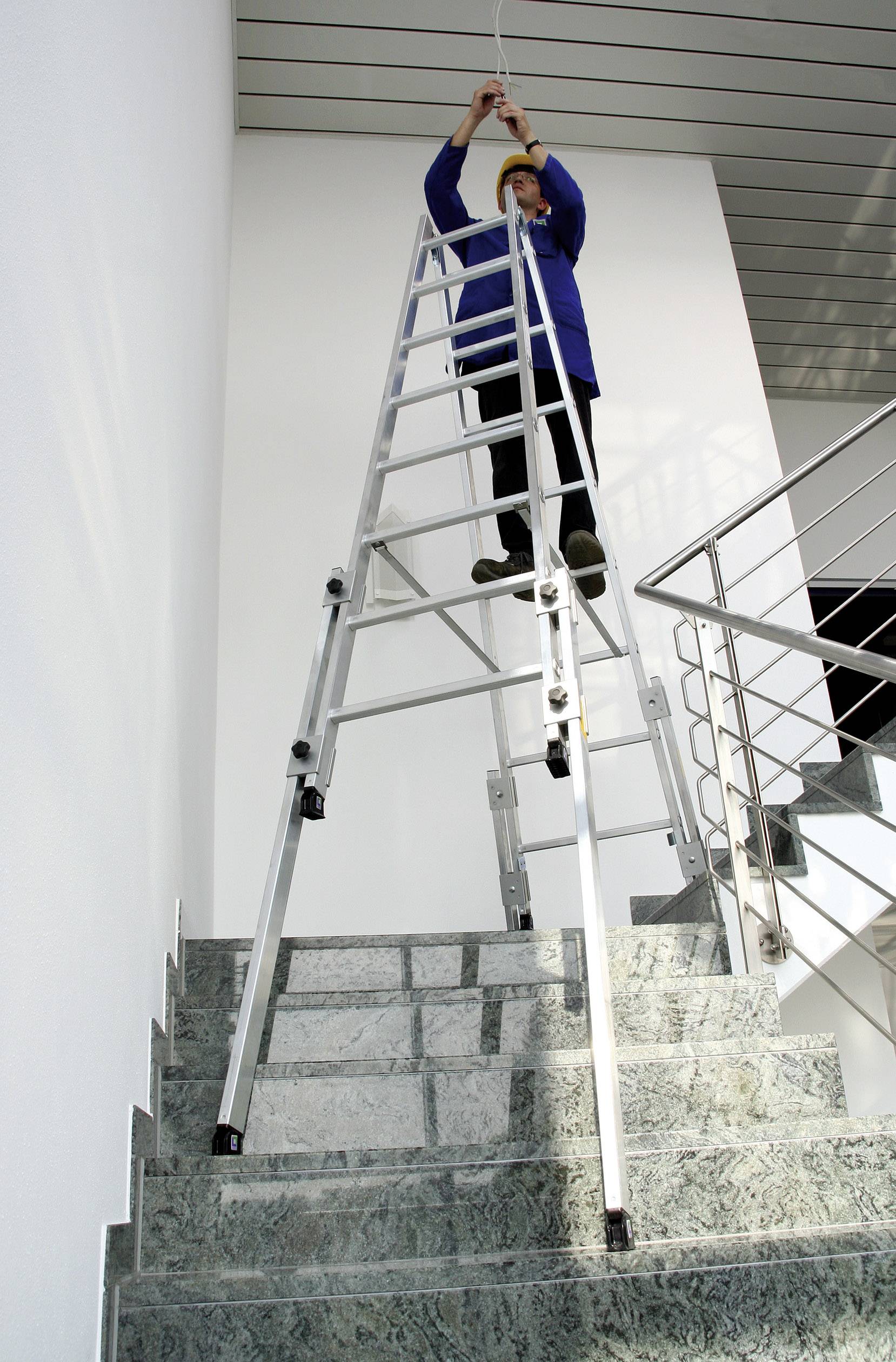 Person auf Leiter installiert Beleuchtung an hohen Decken über einer Marmortreppe in modernen Gebäude.