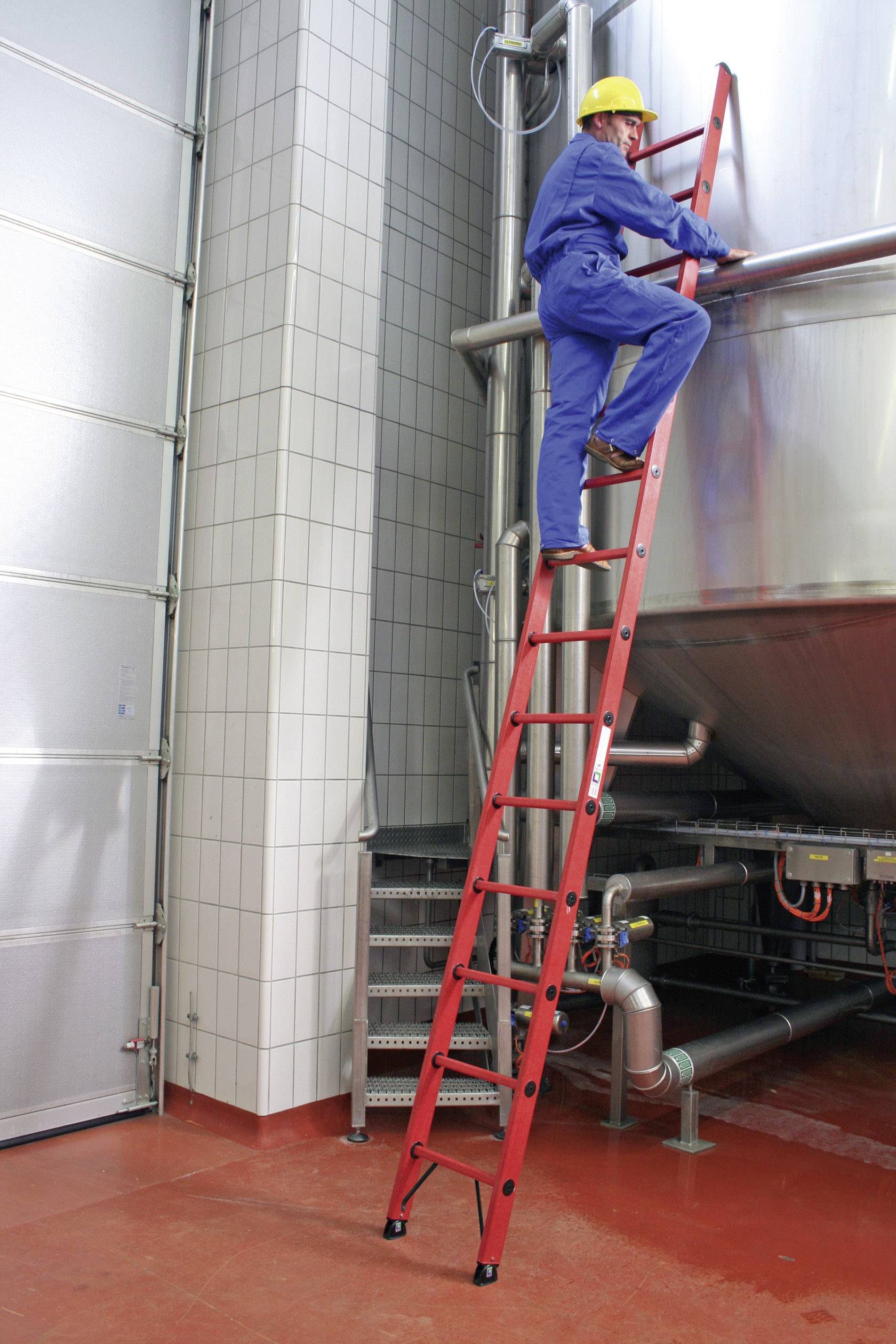 Arbeiter mit gelbem Helm auf roter Leiter neben großem Metalltank in Industrieumgebung.