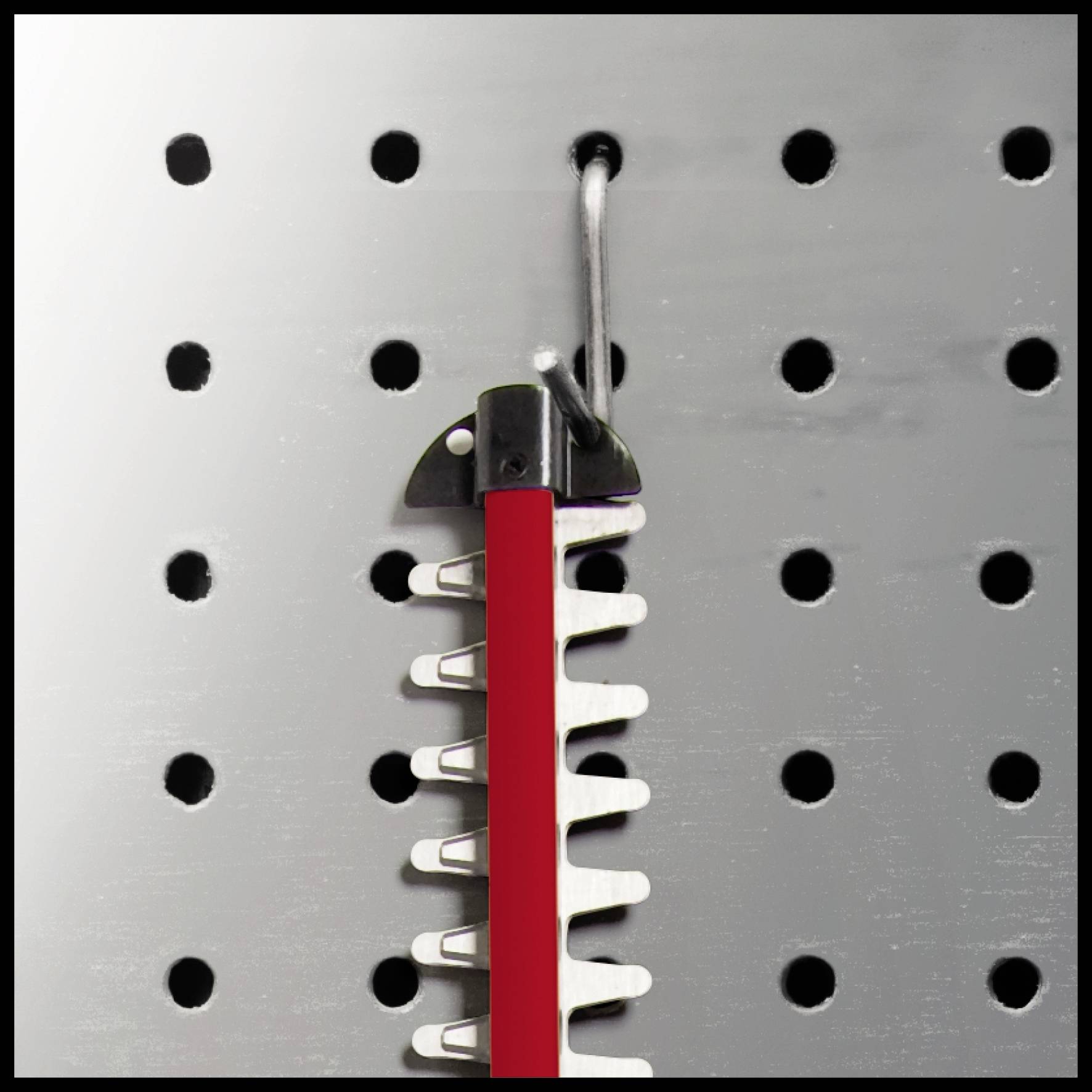 Ein rot-schwarzer Kamm hängt an einem Haken an einer perforierten Metallwand.