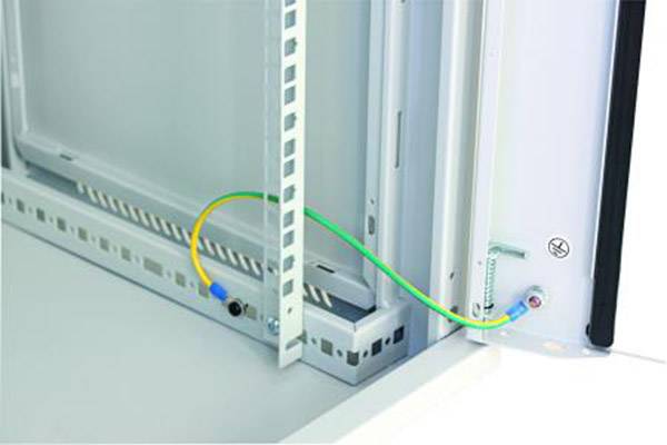 Ein grünes und gelbes Erdungskabel verbindet zwei Metallflächen in einem Elektronikschrank, um eine sichere elektrische Erdung zu gewährleisten.