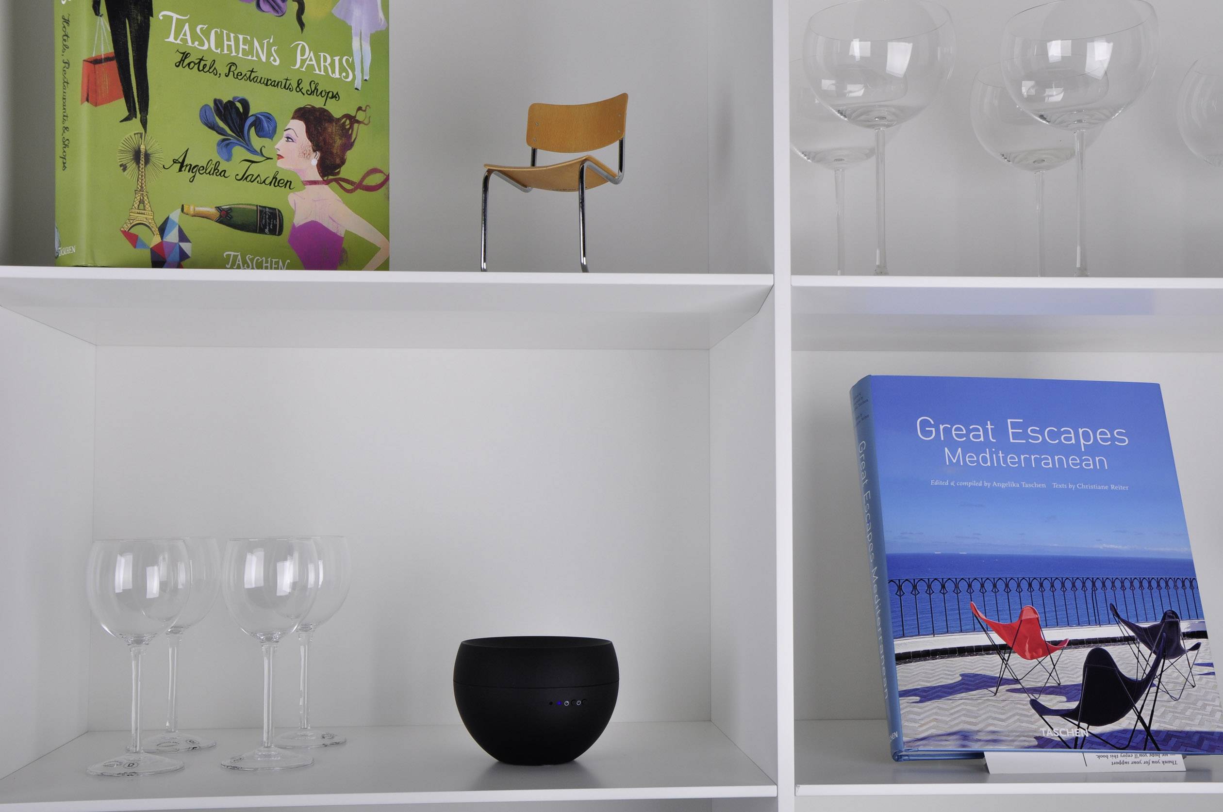 Regal mit Büchern und Gläsern. Unten rechts der Titel 'Great Escapes Mediterranean'. Oben links 'Taschen's Paris'.