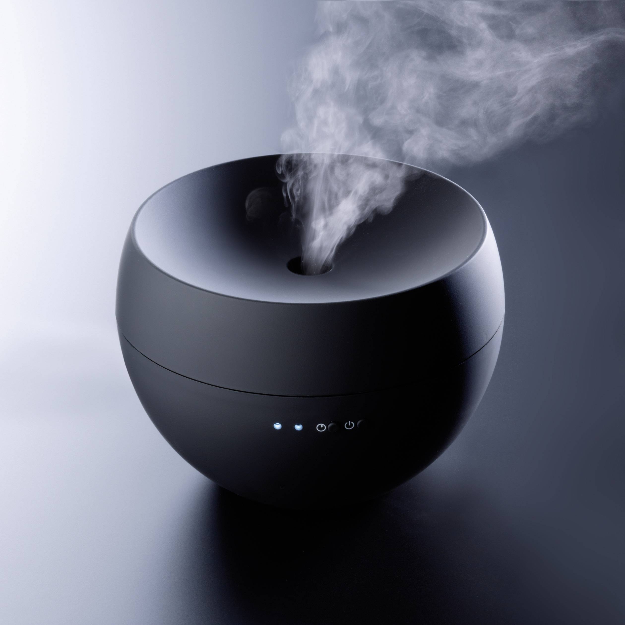 Ein schwarzer, runder Aromadiffuser verströmt Dampf. Drei blaue LED-Lichter sind an der Vorderseite sichtbar.