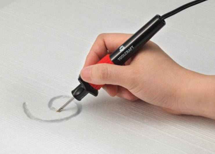 Eine Hand hält eine rot-schwarze Gravurmaschine und graviert einen Kreis auf eine glatte, graue Oberfläche.