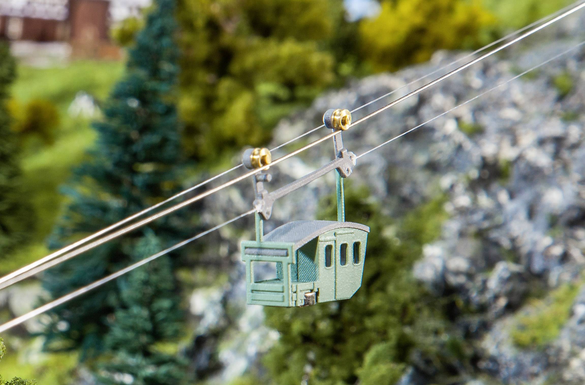 Eine Miniatur-Seilbahn fährt über eine modellierte Berglandschaft mit Bäumen und Felsen im Hintergrund.