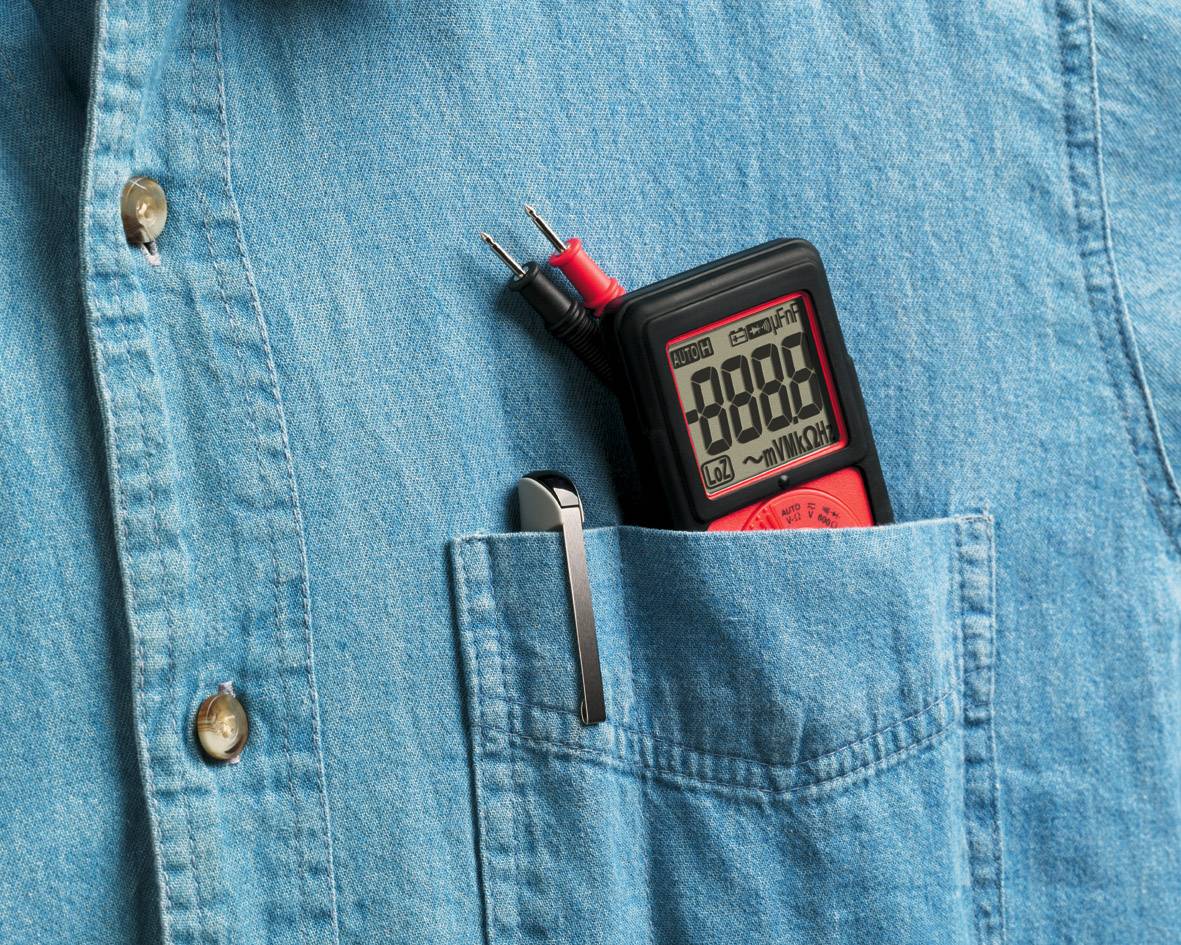 Ein Multimeter steckt in der Brusttasche eines blauen Hemdes. Es zeigt '8888' auf dem Display an. Daneben steckt ein Stift.