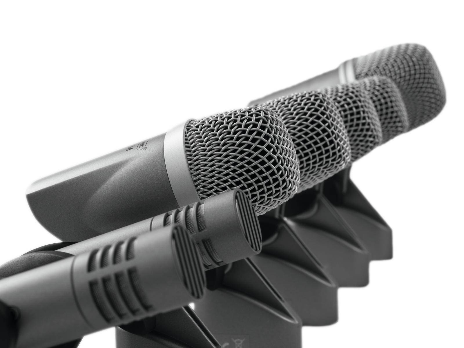 Mehrere Mikrofone in einer Reihe. Die Mikrofone haben metallische Gitter und schwarze Gehäuse und sind in einer Aufnahmesituation angeordnet.