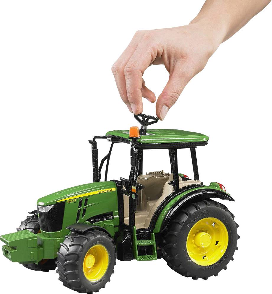 Eine Hand hält ein kleines, grünes Spielzeugtraktorlenkrad. Der Traktor hat gelbe Räder und schwarze Details.
