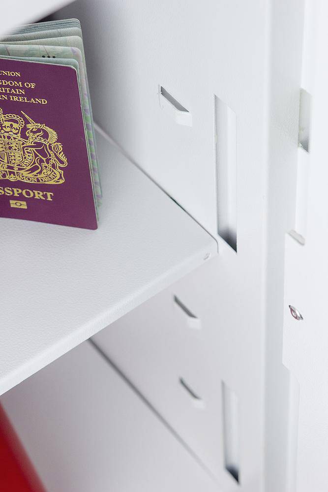 Ein Reisepass mit royalem Wappen liegt auf einem weißen Regal. Teile eines Schließfachsystems sind im Hintergrund sichtbar.