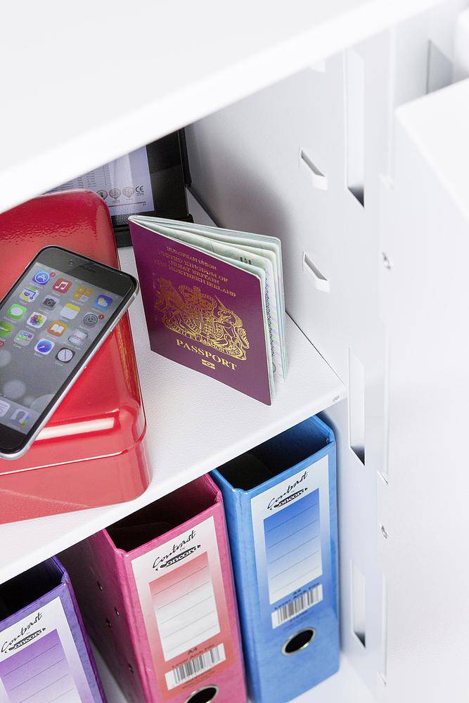 Ein geöffneter Safe zeigt einen Reisepass, ein Smartphone, eine rote Box und farbige Ordner.