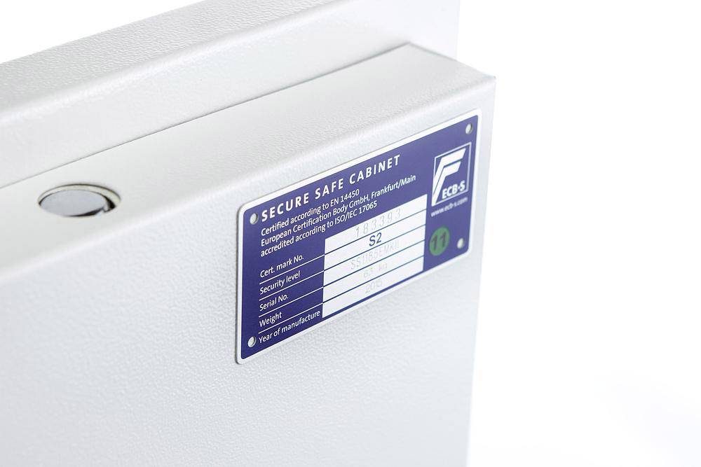 Ein Metallschrank mit einem Etikett 'Secure Safe Cabinet', das Sicherheitszertifizierungen und Seriennummern beschreibt.