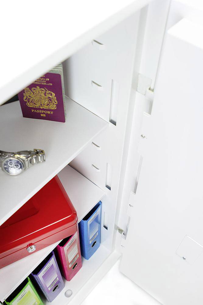 Ein geöffneter Safe mit einem Reisepass, einer Armbanduhr, einer roten Box und mehreren Ordnern in verschiedenen Farben.