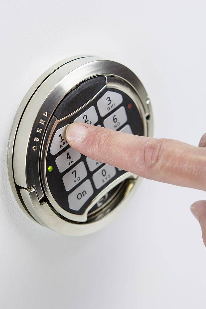 Finger drückt eine Taste auf einem digitalen Zahlenschloss an einem Safe.