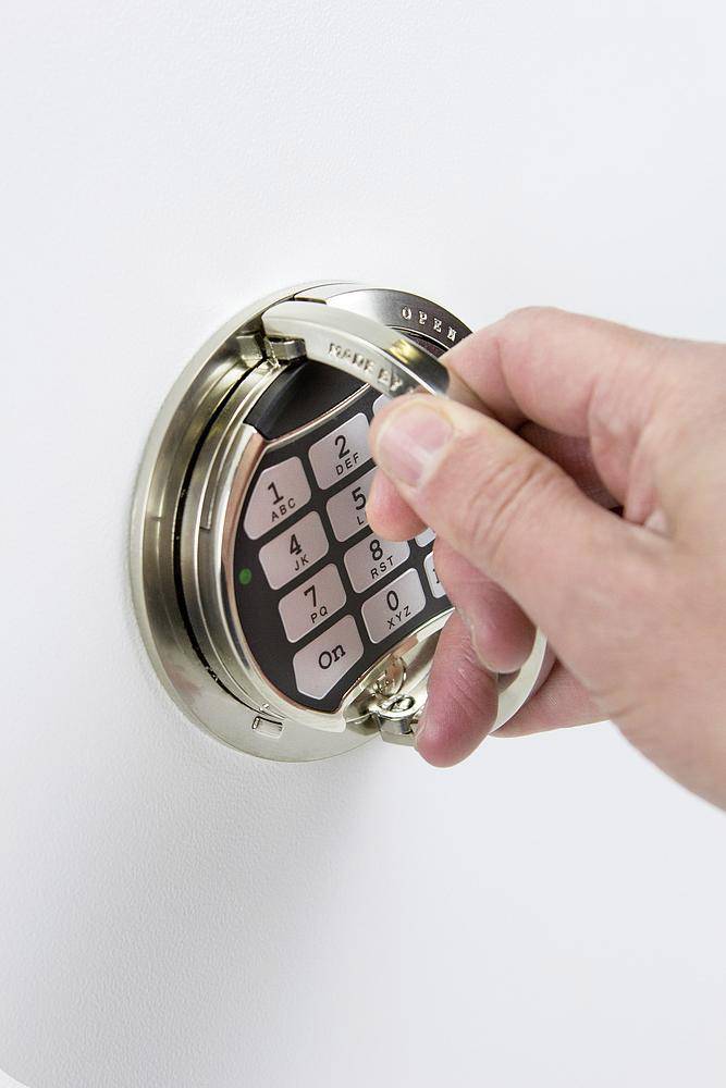 Eine Hand dreht den Schalter eines Tresors mit einem digitalen Tastenfeld; symbolisiert Sicherheit und Zugangskontrolle.