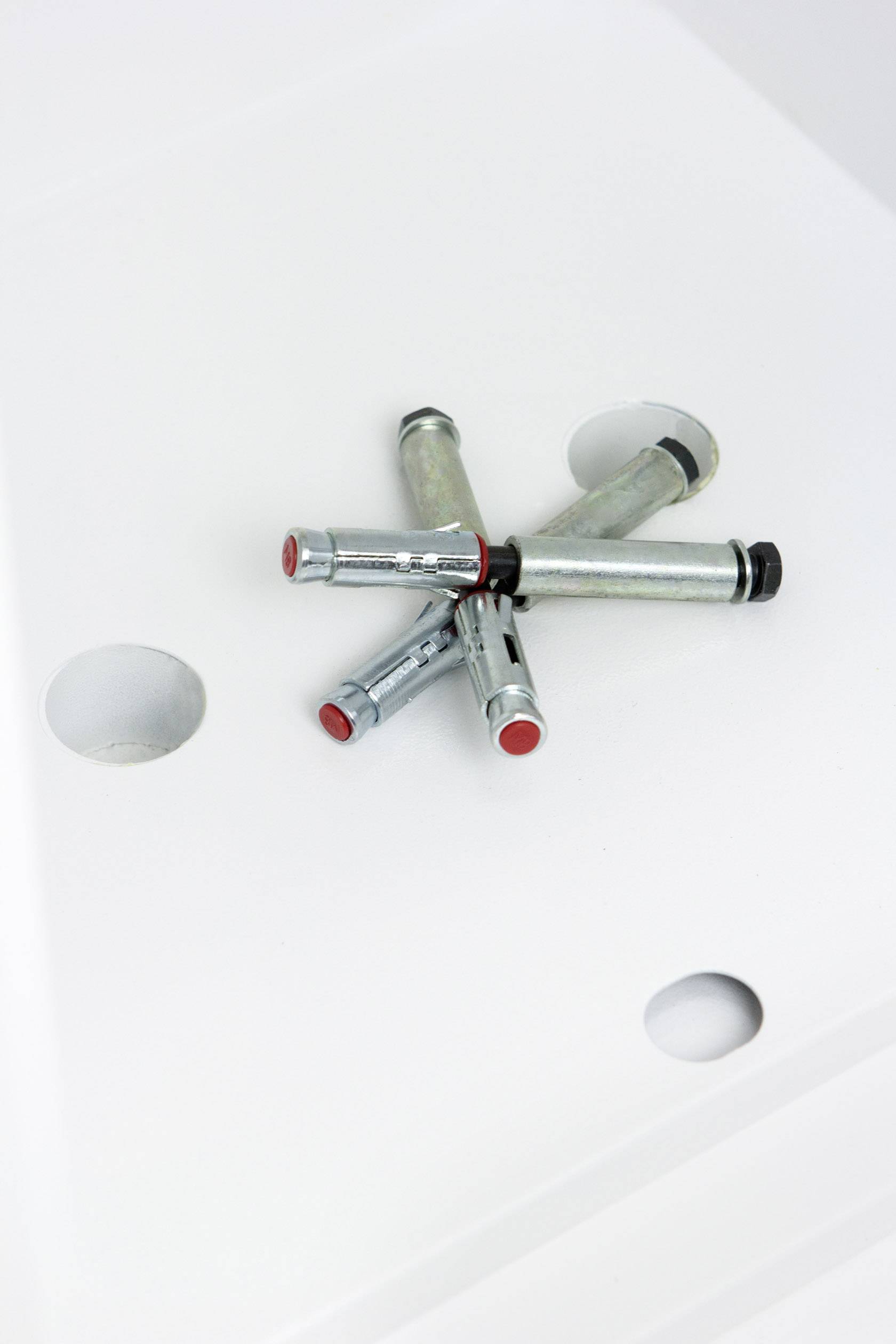 Mehrere silberne Metallstifte mit roten Spitzen liegen kreuzförmig auf einer weißen perforierten Oberfläche.