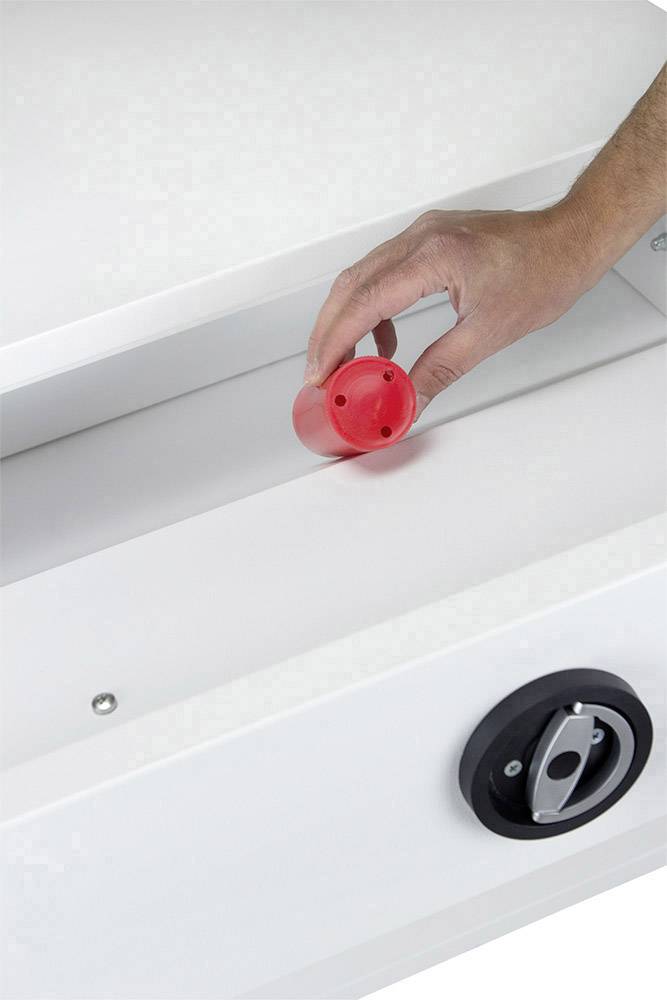 Eine Hand platziert ein rotes Plastikzylinder-Objekt in eine weiße, längliche Halterung. Unten rechts ist ein schwarzes Steuerungsrad sichtbar.