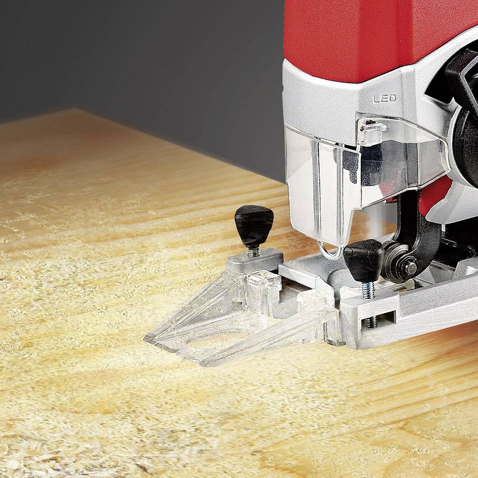 Eine rote Stichsäge schneidet mit einem Sägeblatt durch Holz. Das Gerät ist mit 'LED' gekennzeichnet und arbeitet auf einer Werkbank.