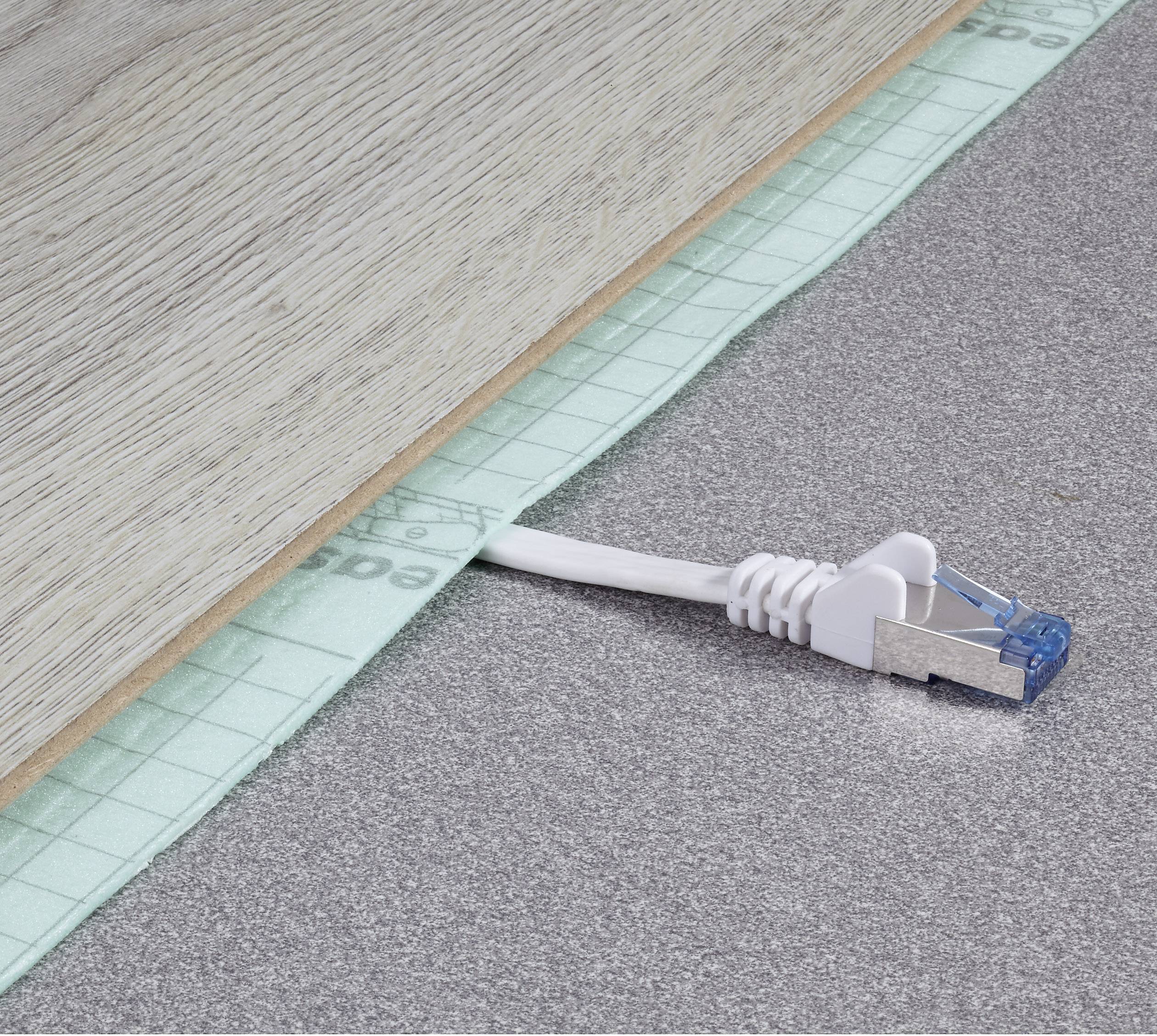 Ein Ethernet-Kabel ragt unter einem Holzbrett auf grauem Boden hervor. Es scheint, als ob das Brett gerade verlegt wird.