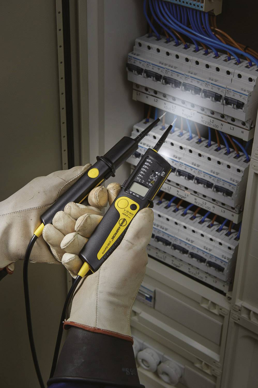 Ein Elektriker mit Schutzhandschuhen verwendet ein digitales Multimeter, um Strom in einem geöffneten Schaltschrank zu prüfen.