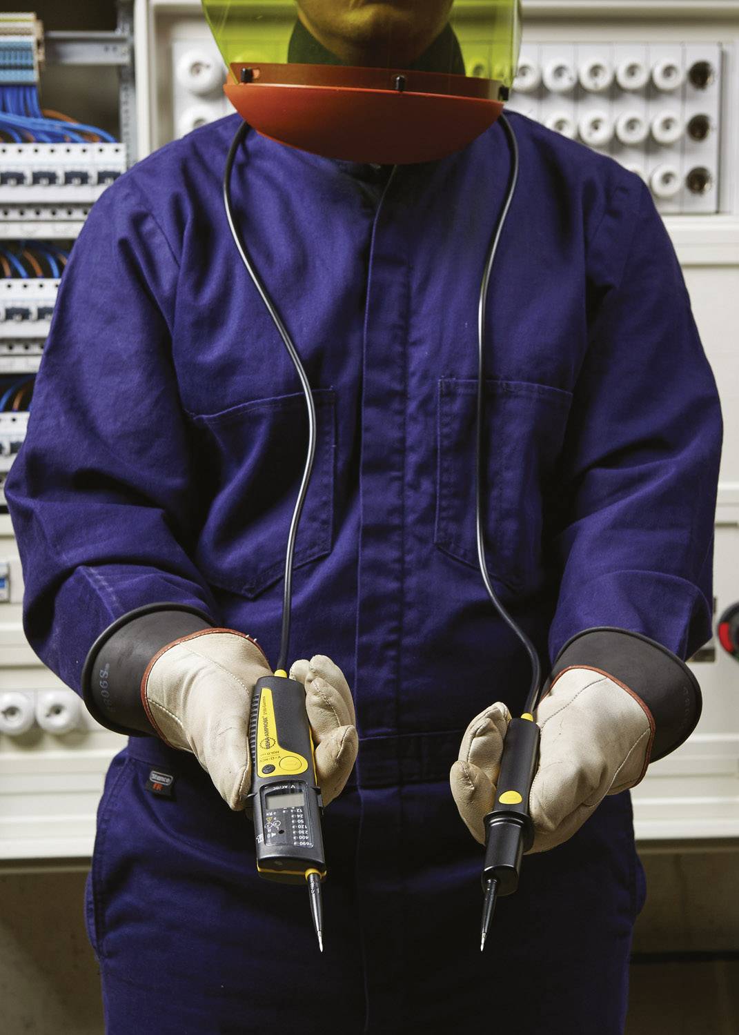 Elektriker in Schutzkleidung hält Spannungsprüfer vor Schaltschrank.