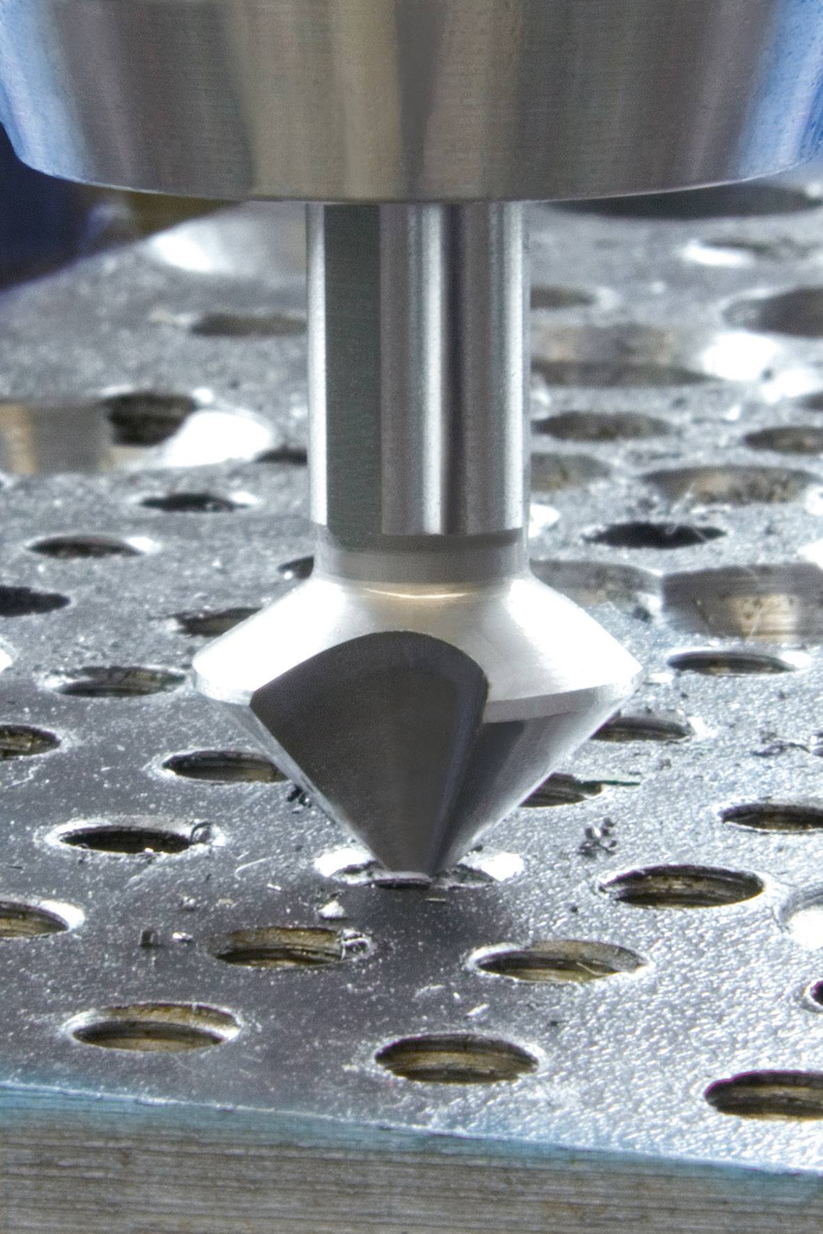Nahaufnahme eines Metallsenkwerkzeugs, das Löcher in eine Metallplatte bohrt. Das Werkzeug hat einen konischen Bohrer.
