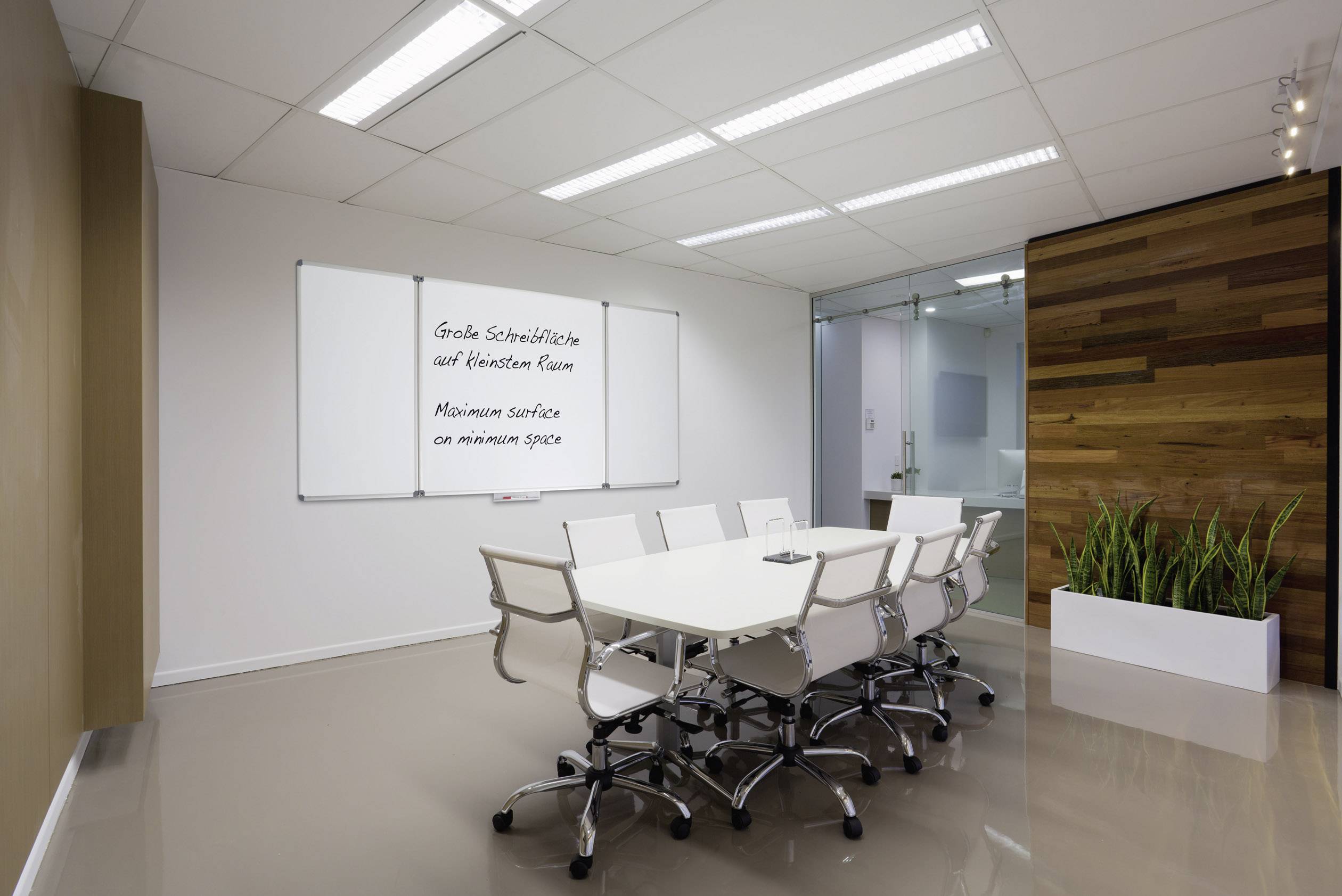 Moderner Konferenzraum mit weißem Tisch, acht weißen Stühlen und einem Whiteboard mit der Aufschrift 'Große Schreibtische auf kleinem Raum'.
