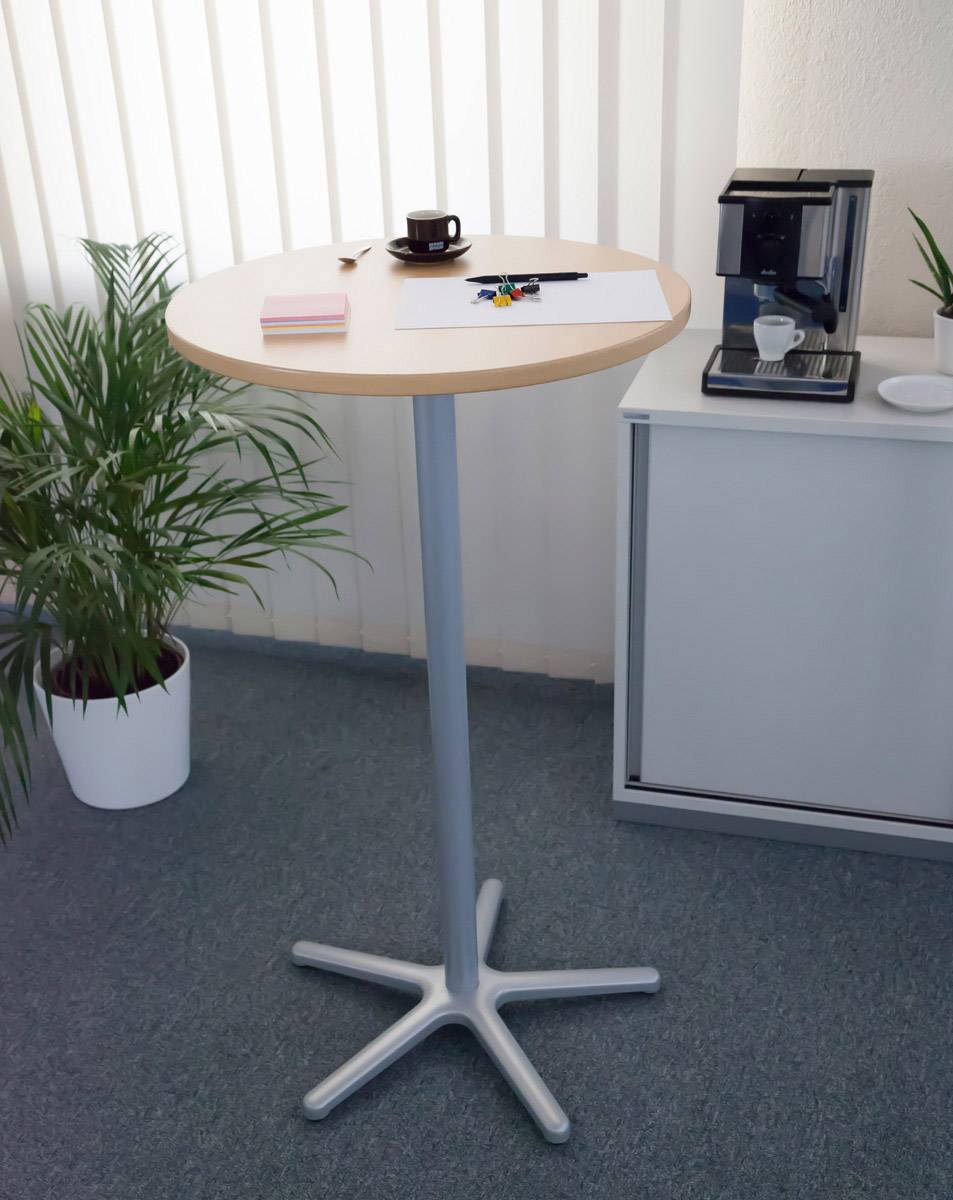 Stehtisch im Büro mit Kaffeetasse, Notizblock und Stiften. Im Hintergrund eine Kaffeemaschine und Pflanzen.