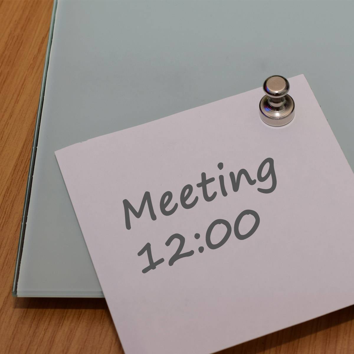 Weiße Notiz auf Schreibtisch, mit einer Klammer befestigt, informiert über ein Meeting um 12:00 Uhr.
