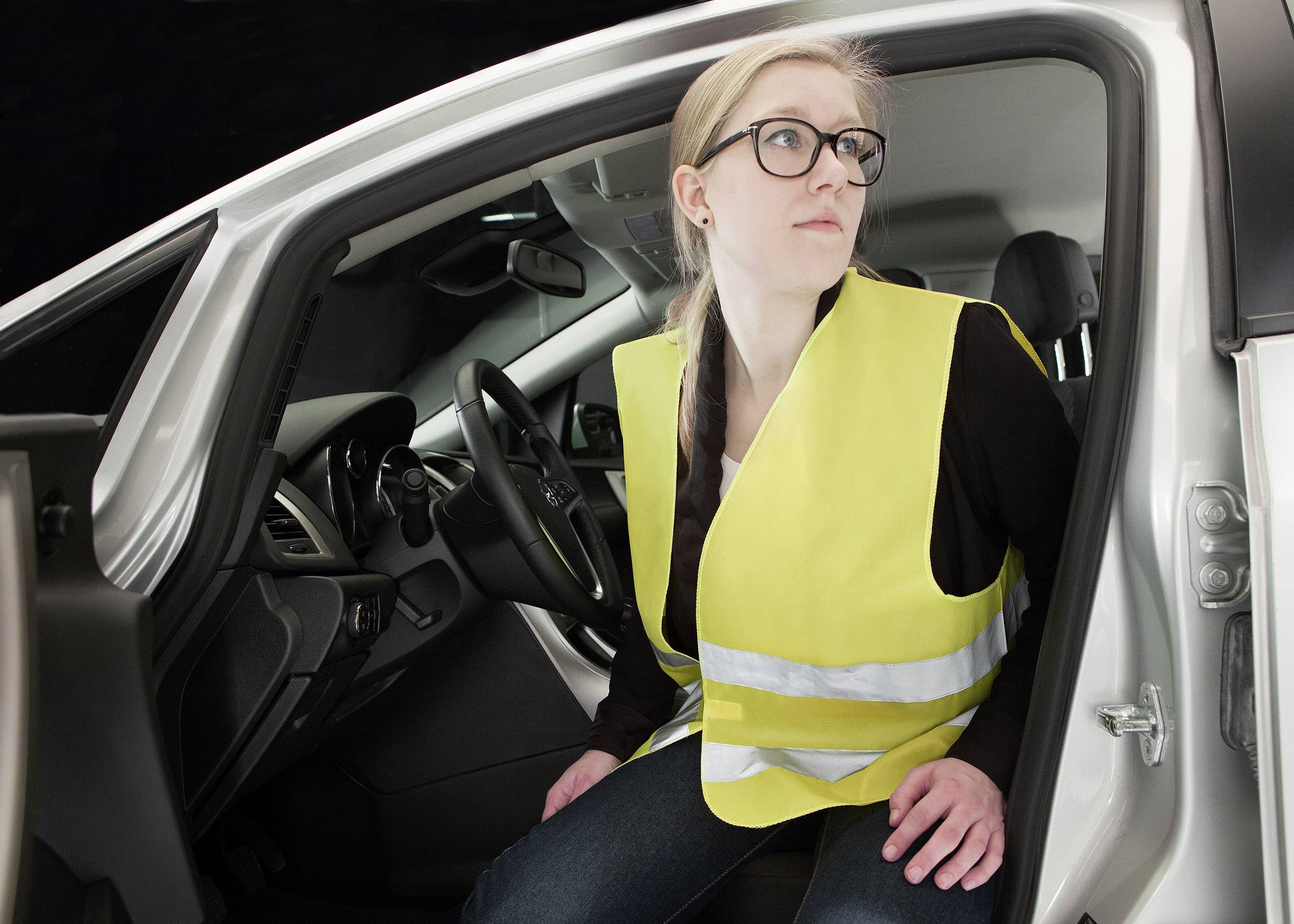 Eine Person mit gelber Warnweste sitzt in einem Auto und blickt nach draußen, als ob sie sich auf das Aussteigen vorbereitet.