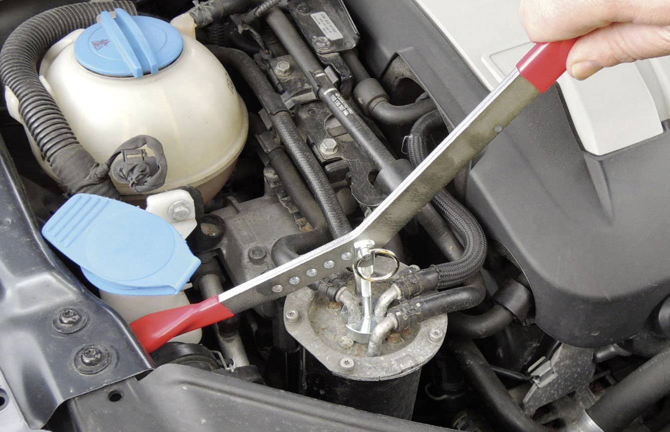 Eine Person verwendet ein Entlüftungsschlüssel, um einen Ölabscheider im Motorraum eines Autos zu öffnen.