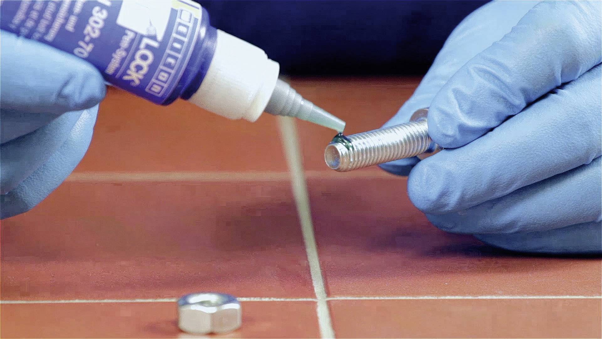 Eine Person mit blauen Handschuhen trägt Klebstoff auf ein Metallgewinde auf, um es zu sichern.