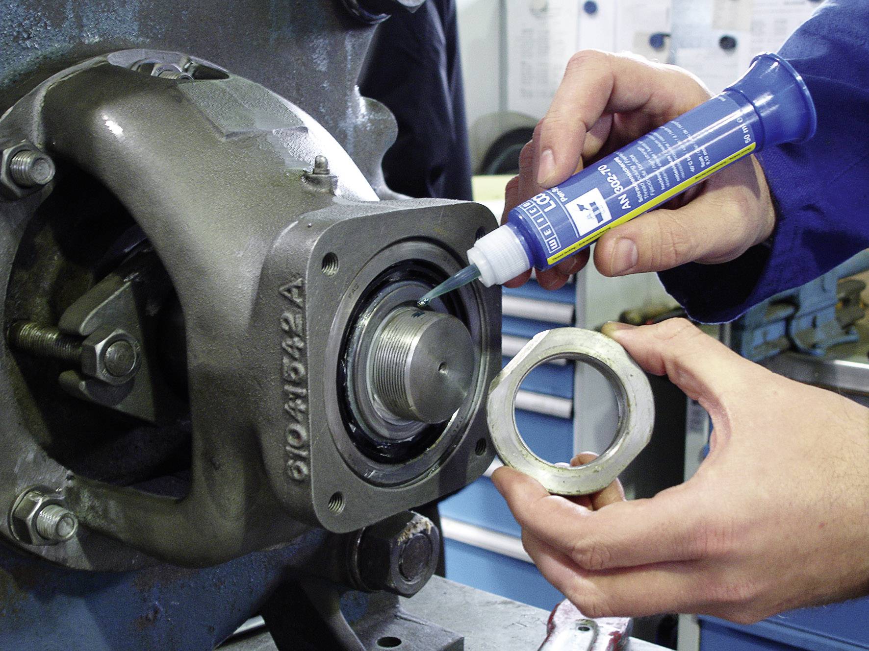 Mechaniker trägt Dichtmasse auf ein Maschinengehäuse auf, während er einen Ring hält. Technik und Präzision in der Wartung.