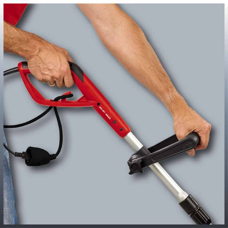 Eine Person hält einen roten Hochdruckreiniger mit schwarzem Kabel. Der Fokus liegt auf der Handhaltung des Geräts.