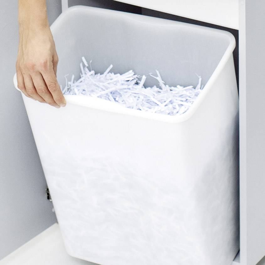 Hand wirft geschreddertes Papier in einen weißen Papierkorb.