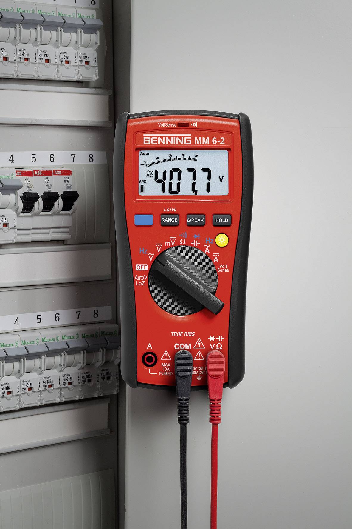 Ein rotes Multimeter zeigt eine Spannung von 40,77 auf einem elektronischen Display an und ist an einem Schaltschrank angeschlossen.