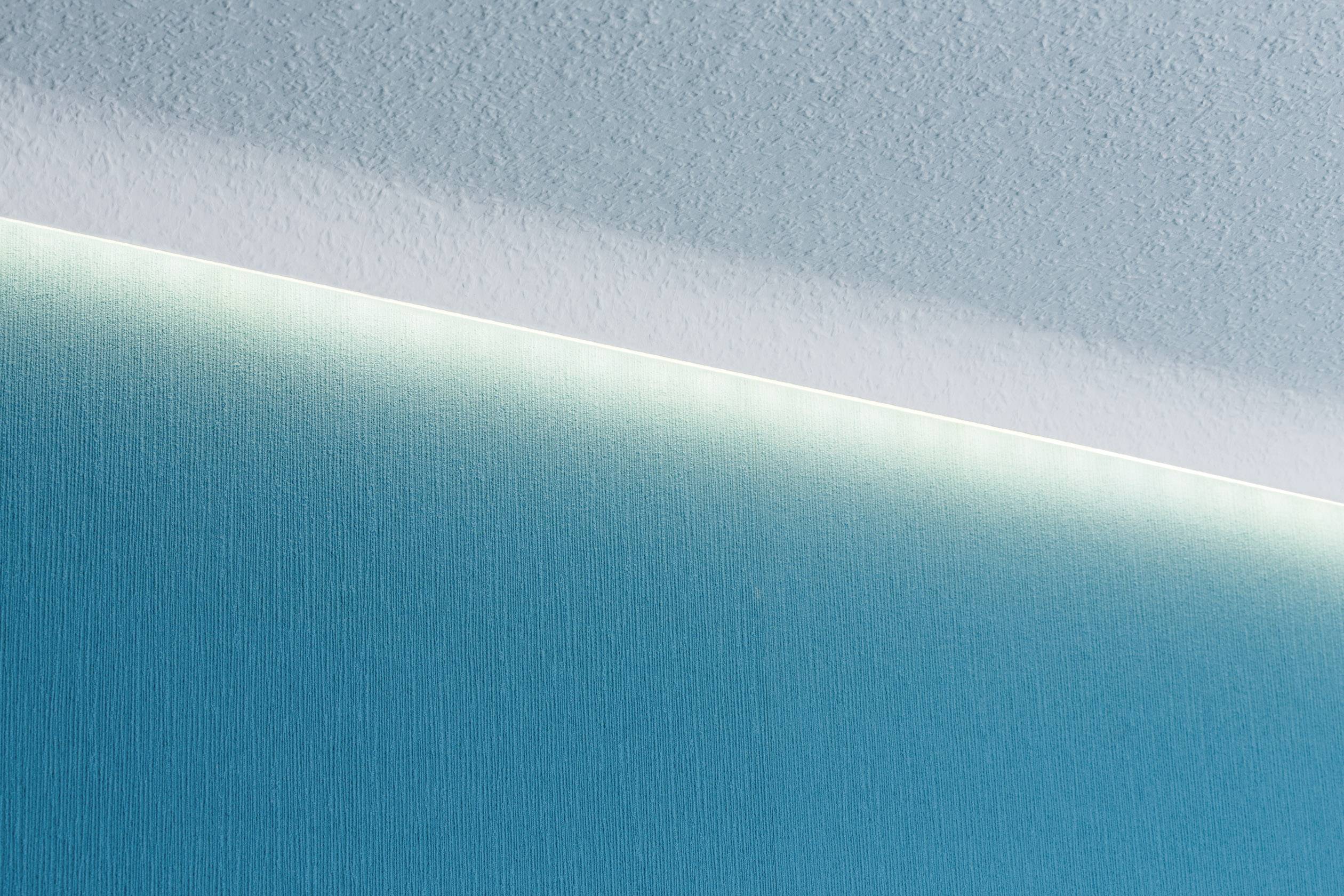 Eine minimalistische Wand mit schrägem Lichtstreifen, der eine subtile Trennung zwischen blauem und weißem Bereich schafft.