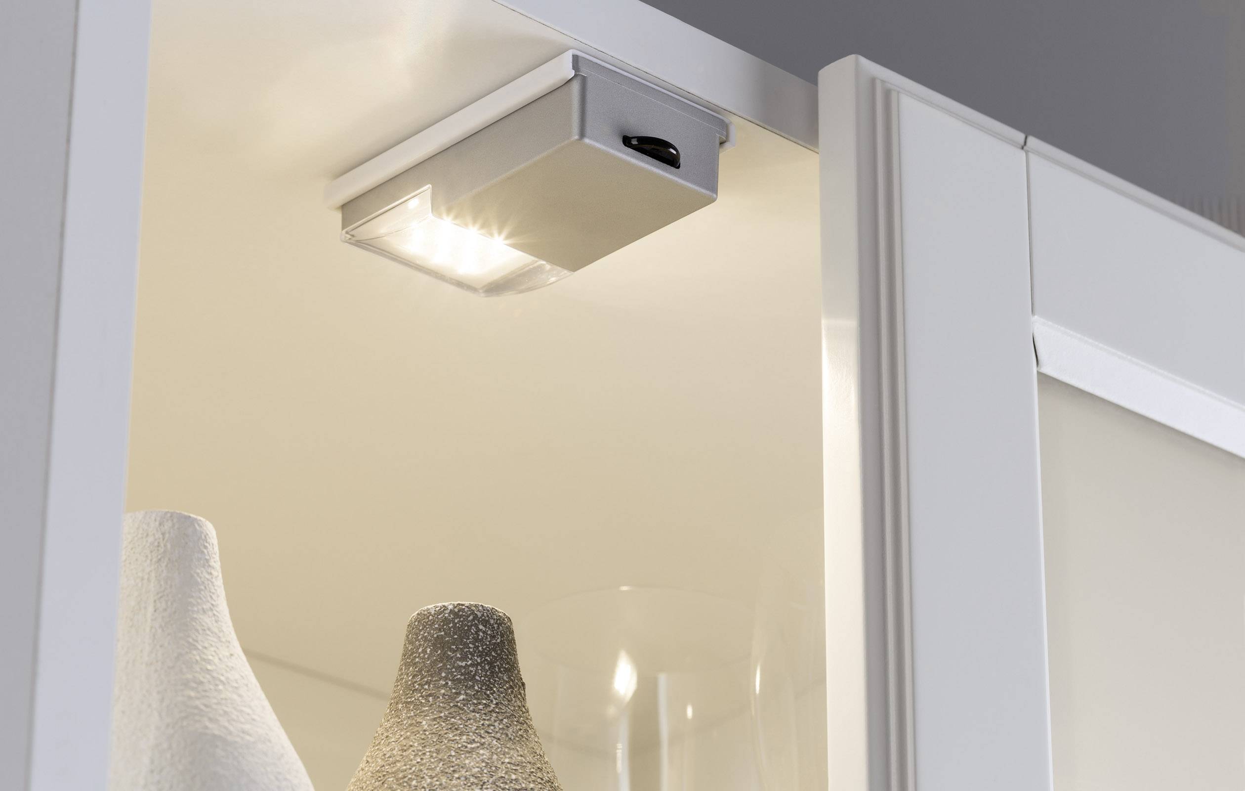 Innenschrankbeleuchtung zeigt einen LED-Spot über weißen Keramikvasen in einem offenen Schrank, sorgt für helles, gerichtetes Licht.